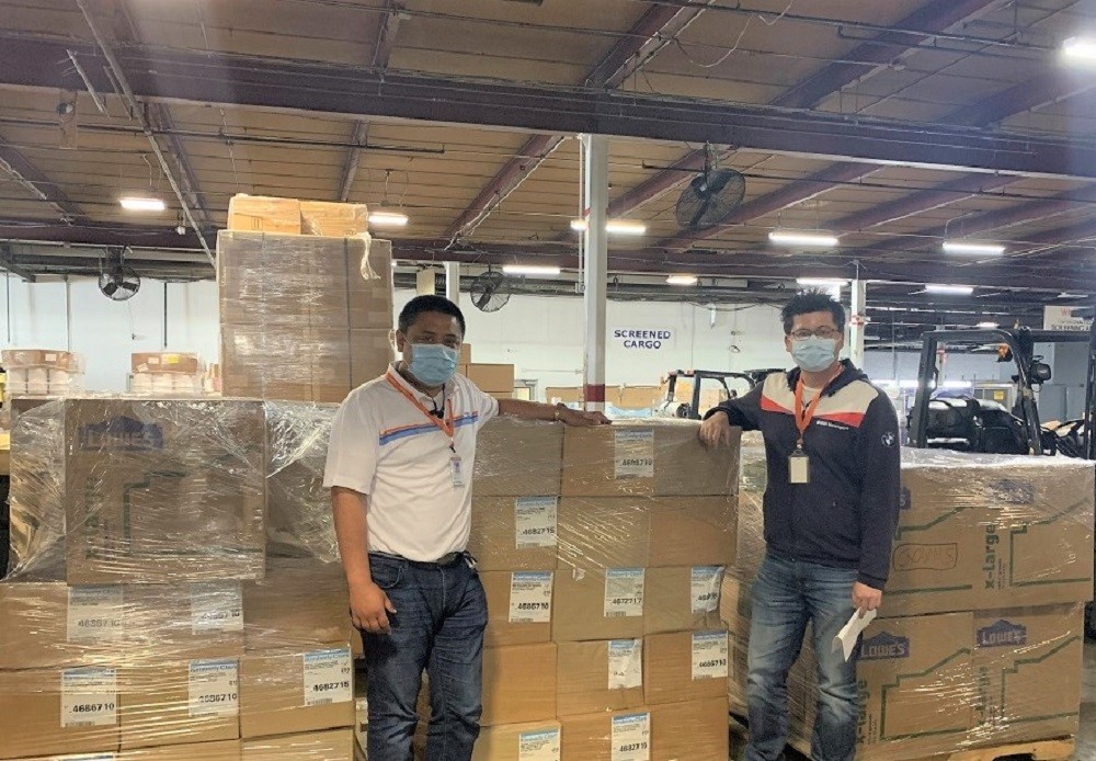 Two Dimerco employees at a warehouse standing next to charitable medical device shipments about to be sent to Bangalore, India.