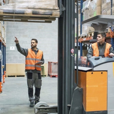 Portrait of two men working in a warehouse, wearing orange vests.