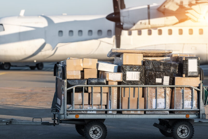 Close-up of a cargo cart full of parcels by a turboprop cargo plane, illustrating air mail shipping and logistics.