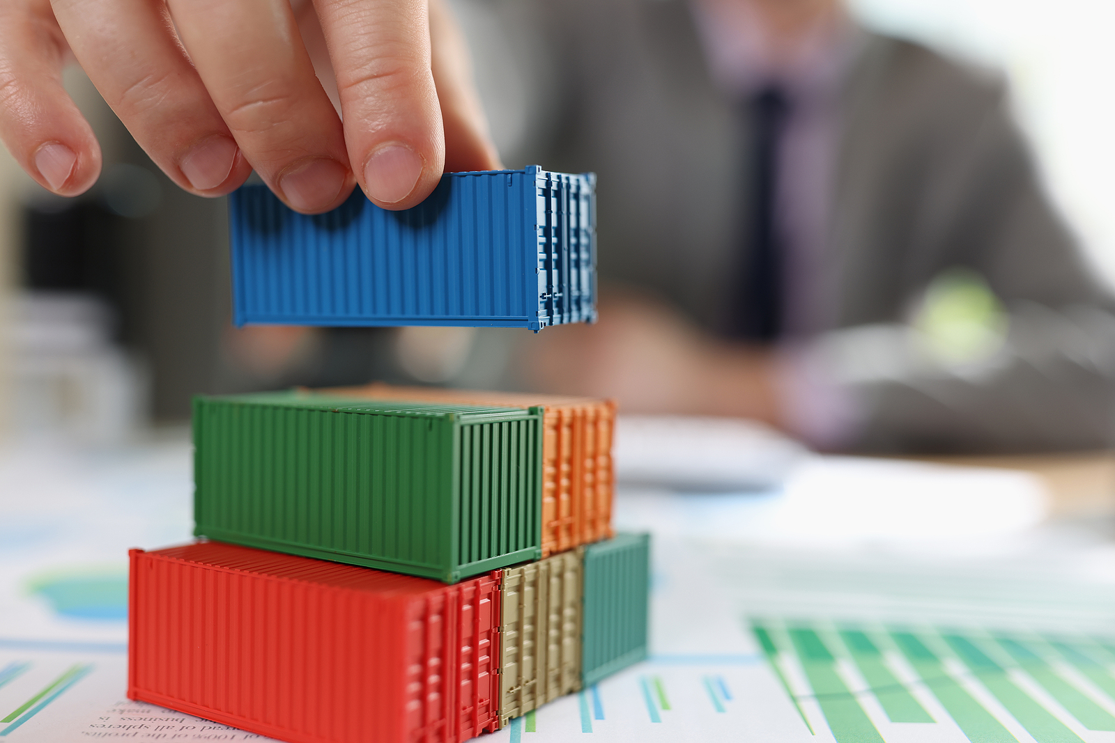 Man stacking cargo containers on financial report papers, symbolizing global logistics and trade.