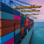 A large container ship docked at a port during sunset, with cranes unloading colorful shipping containers—illustrating freight market uncertainty in 2025