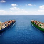 Two large container ships, one blue and one green, sail side by side on the open ocean, representing global shipping alliances and international trade routes.