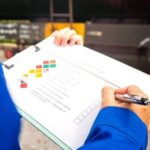 A logistics professional in a blue uniform reviews a Material Safety Data Sheet (MSDS) on a clipboard