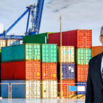 Dimerco CEO Jeffrey Shih standing in front of colorful stacked shipping containers at a port, highlighting leadership amid global supply chain pressures.