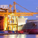 A cargo ship at port next to cranes and shipping containers