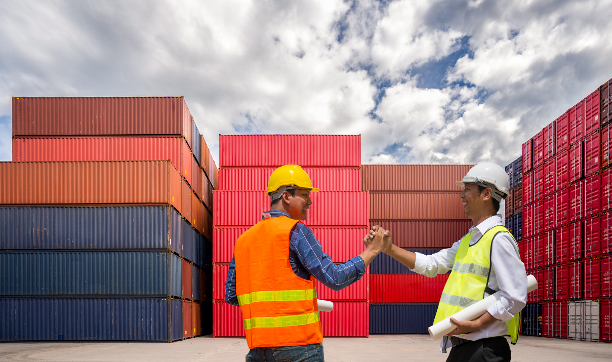 Two logistics professionals shaking hands in front of shipping containers, symbolizing strategic partnerships during the 2026 contracting season
