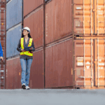 Two logistics professionals walk past shipping containers while discussing CBP enforcement and trade compliance strategy.