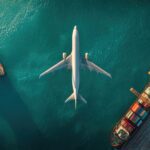 Aerial view of an airplane flying over cargo ships at a port