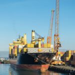 Container ship docked beside port cranes and stacks of shipping containers
