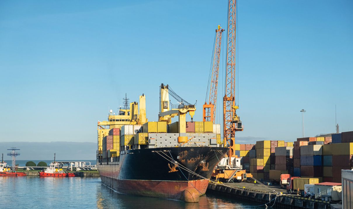 Container ship docked beside port cranes and stacks of shipping containers